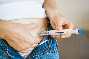 Obraz na płótnie Canvas Woman self-administering GLP-1 medication injection into abdomen