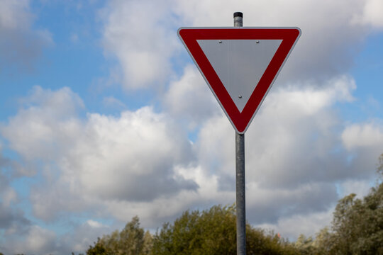 Close-up of a yield traffic sign mounted on a pole against a dramatic cloudy sky. Transportation and road safety concept with ample copy space and clear visual impact.