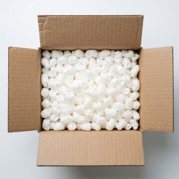 Open cardboard box filled with white packing peanuts. Biodegradable eco friendly foam peanuts provide cushioning for fragile items during shipping. Sustainable packaging material protects parcels in