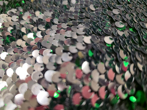 Silver sequins with pink and green reflections close up, shimmering round discs in a festive Christmas and New Year glitter background. Holiday party concept, grainy film texture, high quality photo