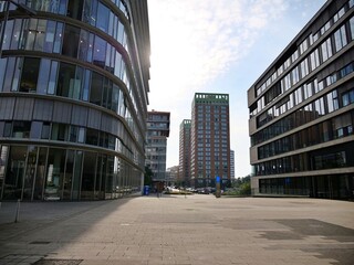 Contemporary city square surrounded by modern glass business buildings and high-rise architecture under soft sunny sky in urban financial district. © Ena