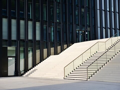 Modern Architecture: Wide Concrete Stairs leading to a Black Glass Office Building with Glass Railings on a Sunny Day.