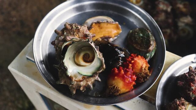 Fresh seafood caught by Korean haenyeo divers, Jeju island, Jeju-do, South Korea, horned turban shells (Turbo cornutus, sora), abalone, sea cucumber and sea squirt on plates and grilled on charcoal