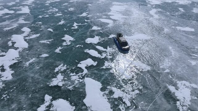 Aerial footage of a modern hovercraft cruising across the cracked blue ice of Lake Baikal in Irkutsk Oblast, Russia during cold sunny winter journey over endless snowy expanse