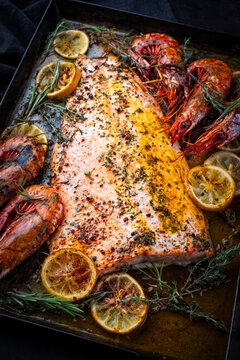 Oven baked salmon filet spicy roast with white tiger prawns, herbs and lemon slices served as close-up on a baking roast tray