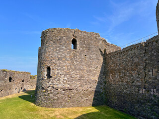 Beaumaris Castle, Isle of Anglesey, - july 17, 2026: A round stone tower and crenellated curtain wall of a medieval castle rise above a grass-covered ward under a clear blue sky, with a metal railing © AnyaWhy