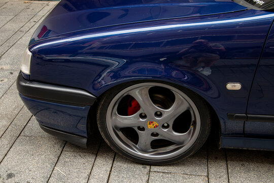 GANDIA, SPAIN - OCTOBER 4, 2026. Front fender and custom Porsche alloy wheel on a lowered dark blue modified car parked on the street.