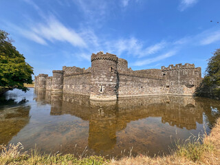Beaumaris Castle, Isle of Anglesey, - july 17, 2026: Medieval stone castle with round corner towers and crenellated walls surrounded by a water-filled moat that reflects the structure under a blue sky © AnyaWhy