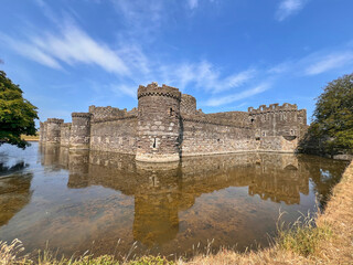 Beaumaris Castle, Isle of Anglesey, - july 17, 2026: Medieval stone castle with round corner towers and crenellated walls is reflected in the still water of a surrounding moat under a blue sky with wi © AnyaWhy