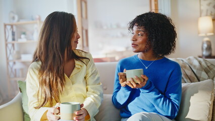 Naklejka premium Multiracial friends drinking coffee sofa. Two women chatting home morning.