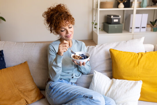 Woman eating healthy breakfast on sofa enjoying morning
