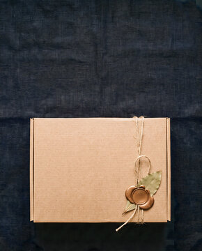 Rustic kraft gift box with twine and wax seal on dark fabric flat lay