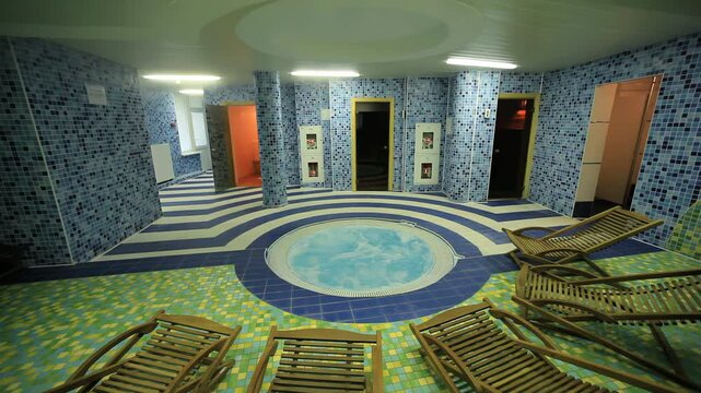 Wooden deck chairs around indoor jacuzzi. Mosaic spa sauna room camera tilt up.