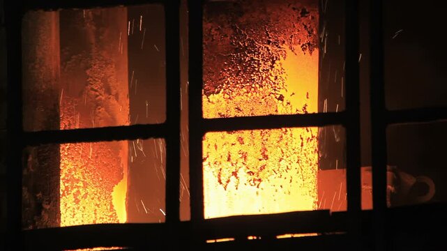 Sparks flying industrial furnace window grid. Steelworks foundry closeup heat.