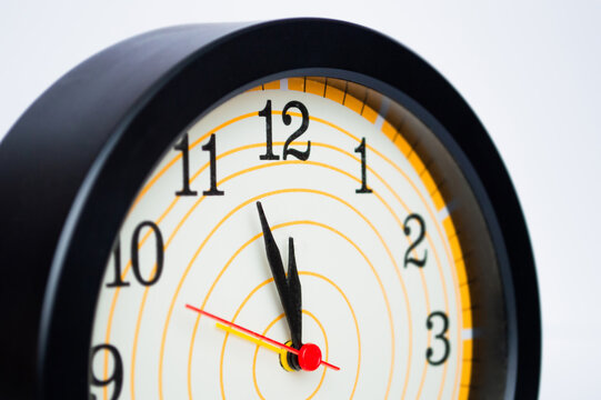 Extreme Close-Up of a Black Analog Wall Clock Showing One Minute to Twelve, with Black and Red Hands and a Cream Dial