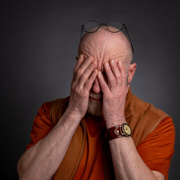 casual portrait of a senior bald man covering his face with hands, tired, stressed or in dispair