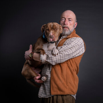 portrait of a serious, bearded senior man hugging his pitbull dog