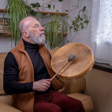 senior man is playing a native American style, shaman drum with a beater at home, lifestyle and hobby concept