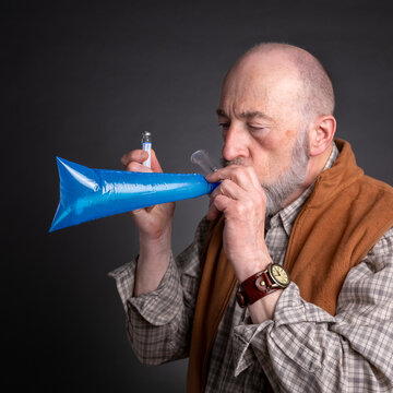 Head and shoulders portrait of a senior man performing breath test to diagnose SIBO (small intestinal bacterial overgrowth)