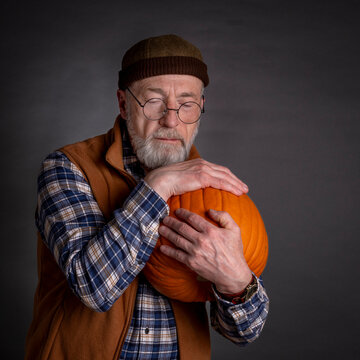 portrait of senior, bearded man hugging a pumpkin. Thanksgiving or Halloween greeting card concept