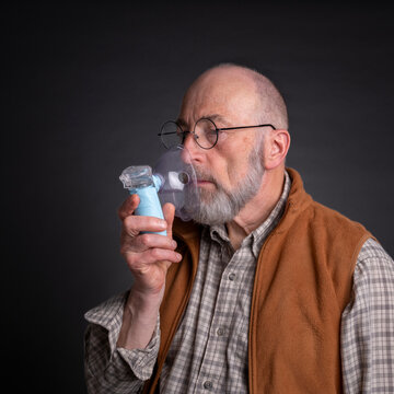 Head and shoulders portrait of a senior man using a portable handheld nebulizer, self care and respiratory therapy concept