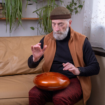 focused senior man is playing steel tongue drum with his hands, lifestyle and hobby concept