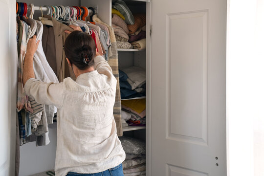 Back view of a woman looking through hanging clothes in a well-stocked closet, deciding what to wear