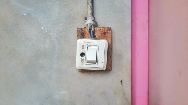 Old electrical light switch mounted on a wooden board against a concrete wall