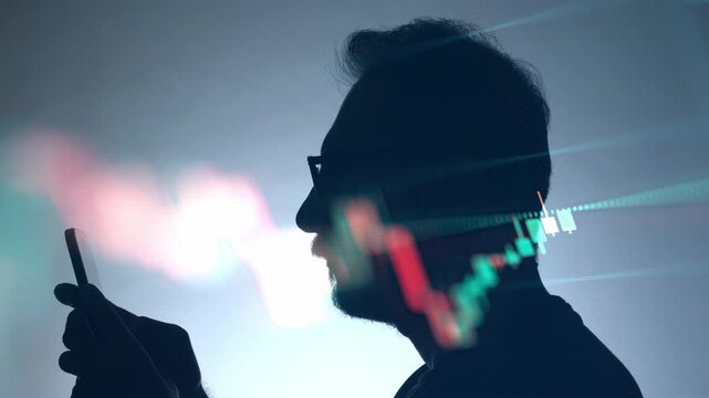 A double exposure video featuring a silhouette of a man using his phone against a white background, blended with a fast moving timelapse of stock market candlestick charts.