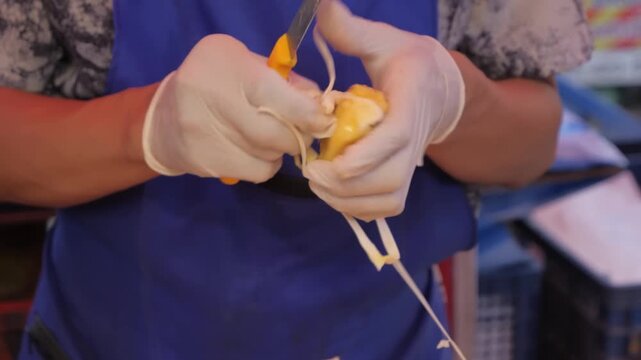 close-up shot of a street vendor wearing protective gloves while skillfully slicing and preparing fresh, ripe jackfruit.