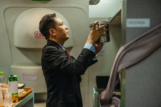 Male flight attendant checking cabin compartment near emergency exit door in airplane