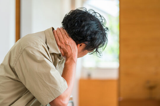 家で首の後ろを押さえて痛みに悩む40代男性。脳梗塞や頸椎の異常・首こりなど健康不安のイメージ