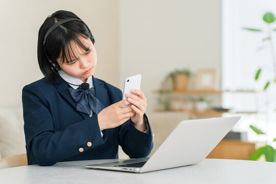 A junior high or high school girl looking worried and struggling with her studies and homework while using a smartphone and computer