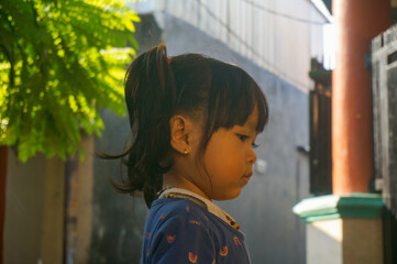 Side profile portrait of cute Asian little girl with ponytail playing outdoors in daylight © Rendi