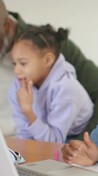 Vertical video: Watching child in purple hoodie leaning at home, adult laughing behind at laptop