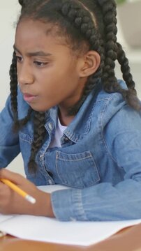 Vertical video: Reading page girl in denim shirt picking pencil and writing at table doing homework