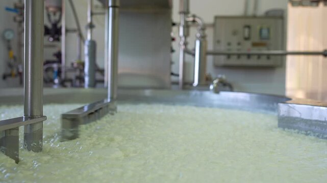 Industrial equipment mixing milk in a large stainless steel tank during the cheesemaking process