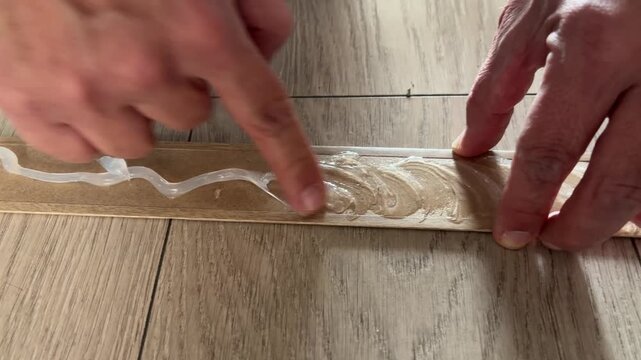 Hand applying silicone glue to skirting board