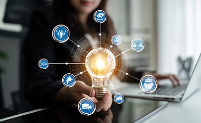 A businesswoman presents a glowing light bulb symbolizing creativity and innovation. Digital icons surround her, representing technology and modern solutions in a contemporary office. Crux © InfiniteFlow