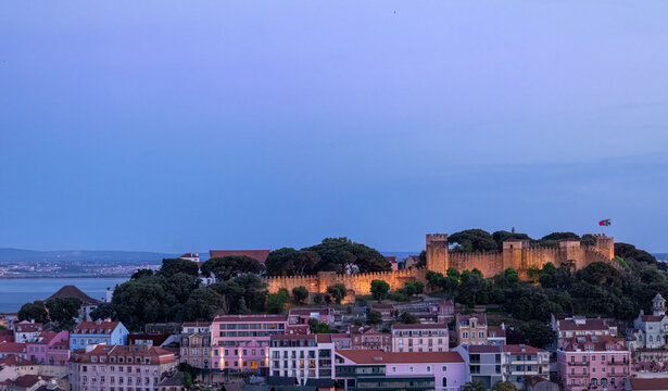 Panoramic sunset view of the Lisbon city skyline showing illuminated Saint George Castle overlooking the Tagus River