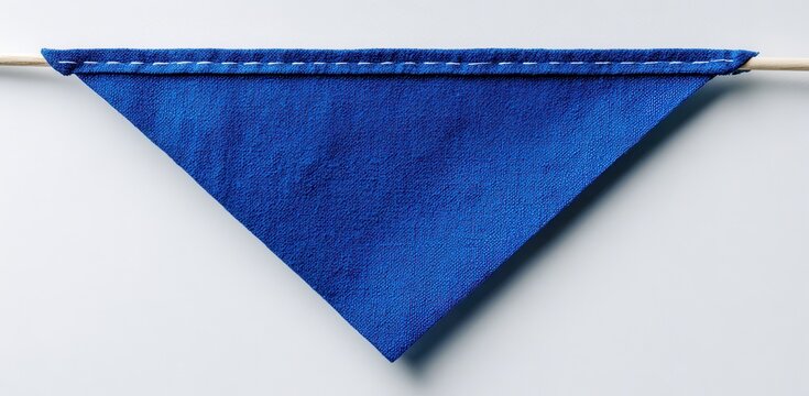Triangular blue textured pennant flag hanging from a wooden stick against a white wall with triangle material background decoration geometry handmade interior minimalist vertical