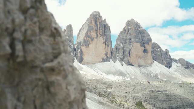 Rough textured rock filling the left half of the frame in close up with the Tre Cime di Lavaredo peaks and snow patches on the slopes below on the right side in the Dolomites Italy