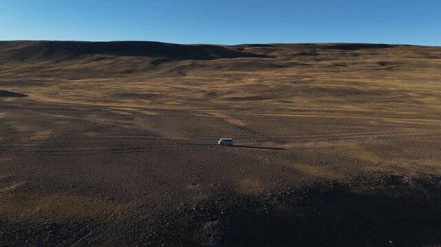 High-altitude aerial drone following a van off road camping vehicle in expansive terrain and rugged wilderness across the Altai Mountains in Mongolia