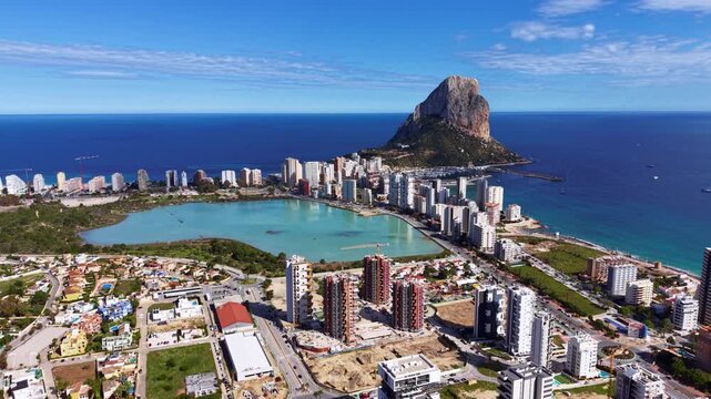 Calpe Spain coastal cityscape with Penon de Ifach rock formation rising above Mediterranean Sea, lagoon, high-rise buildings and blue sky
