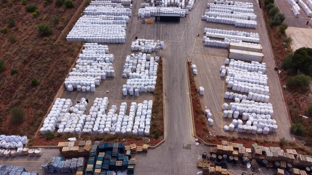 Overhead view of a plastic recycling plant yard with rows of white bulk bags, wooden pallets and crates organized across a large industrial outdoor storage area
