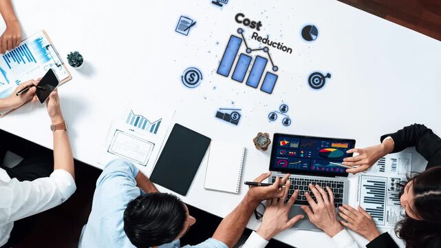 Dynamic scene of a team collaborating to strategize cost reduction with data analysis tools, featuring graphs and digital insights in a modern office environment. Raster