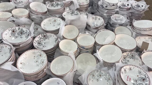 A close-up view of stacked ceramic bowls and floral patterned plates on display. A vast collection of elegant kitchenware featuring porcelain dishes with delicate grey, green, and blue flower motifs 