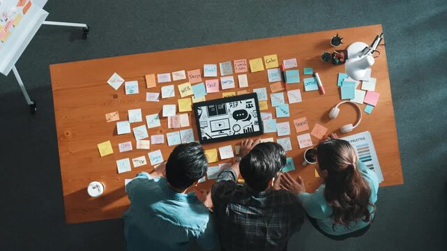 Top view of creative designer working together brainstorming idea by using sticky notes at meeting table with color palettes. Aerial view of smart team choosing icon graphic from tablet. Symposium.