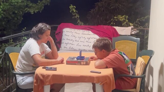 Mother and son playing a board game on a balcony in Kalamata Greece at night
