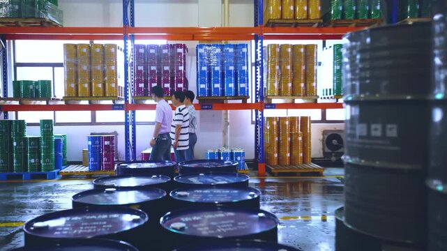 Industrial worker inspectors inspecting stacked green barrels, fuel oil or chemical tanks in a storage facility ensuring proper inventory management and workplace safety